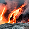 Smoking red lava boiling down a black rocky hillside into steaming slate-blue ocean waves
