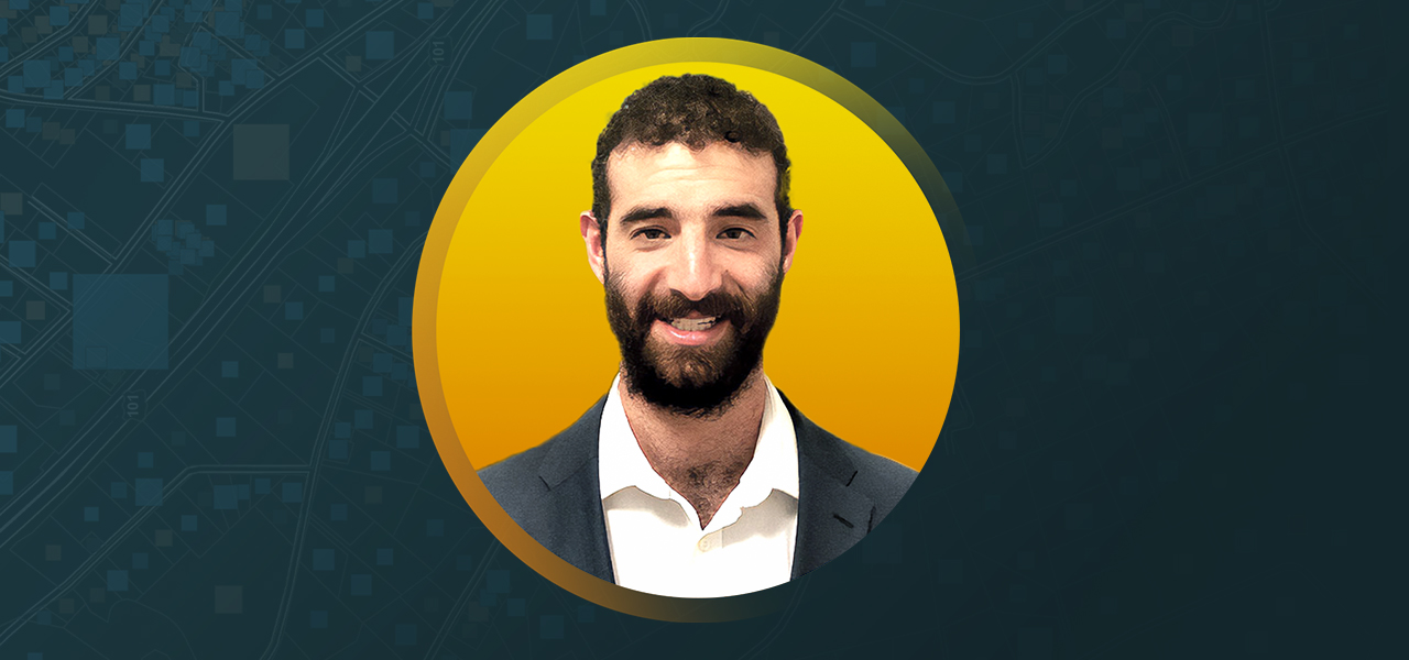 노란색과 파란색 배경에 중첩되어 비즈니스 정장을 입고 웃고 있는 Zach Jaffe
